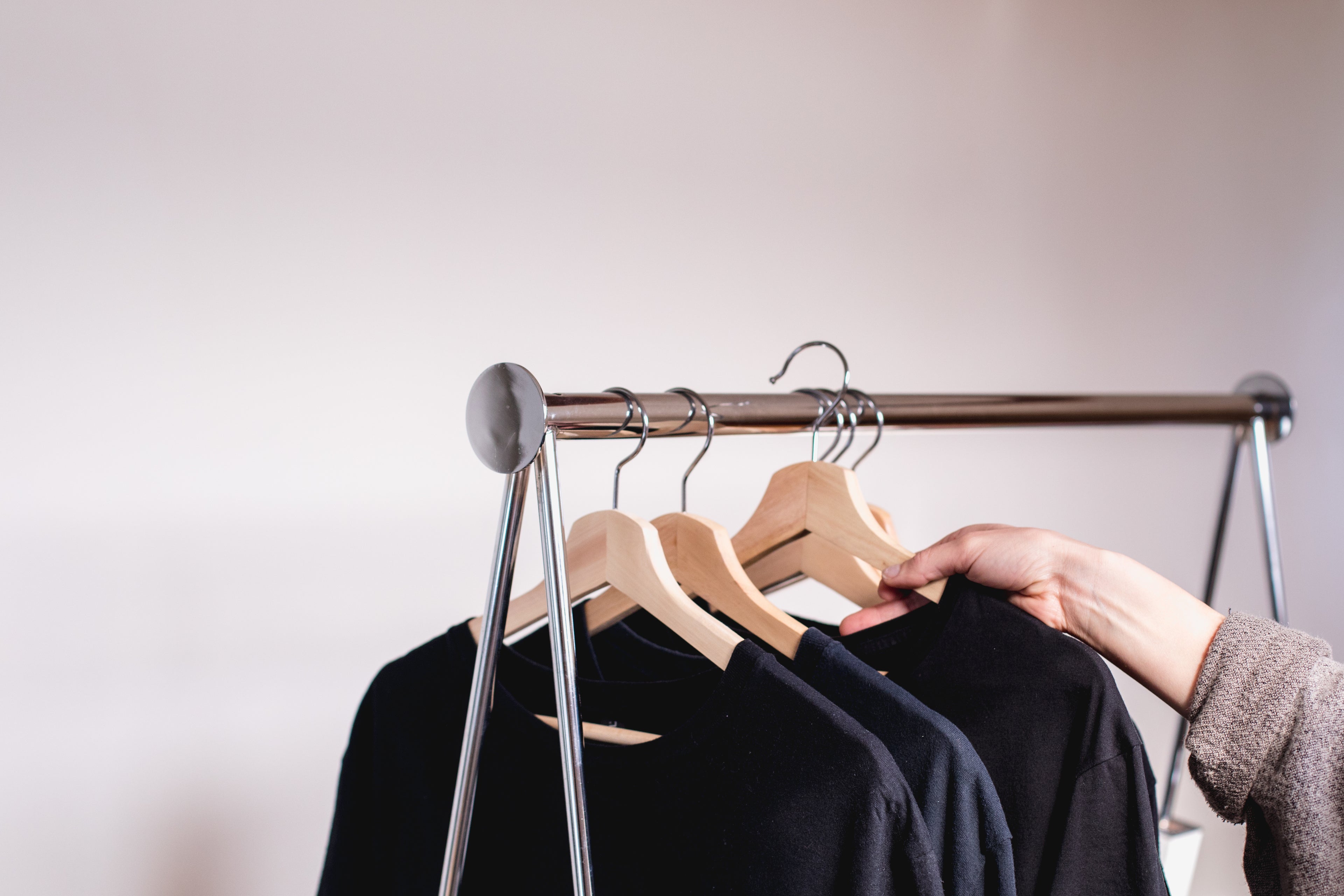 a-hand-removes-a-sweater-from-a-clothing-rack - We Want More